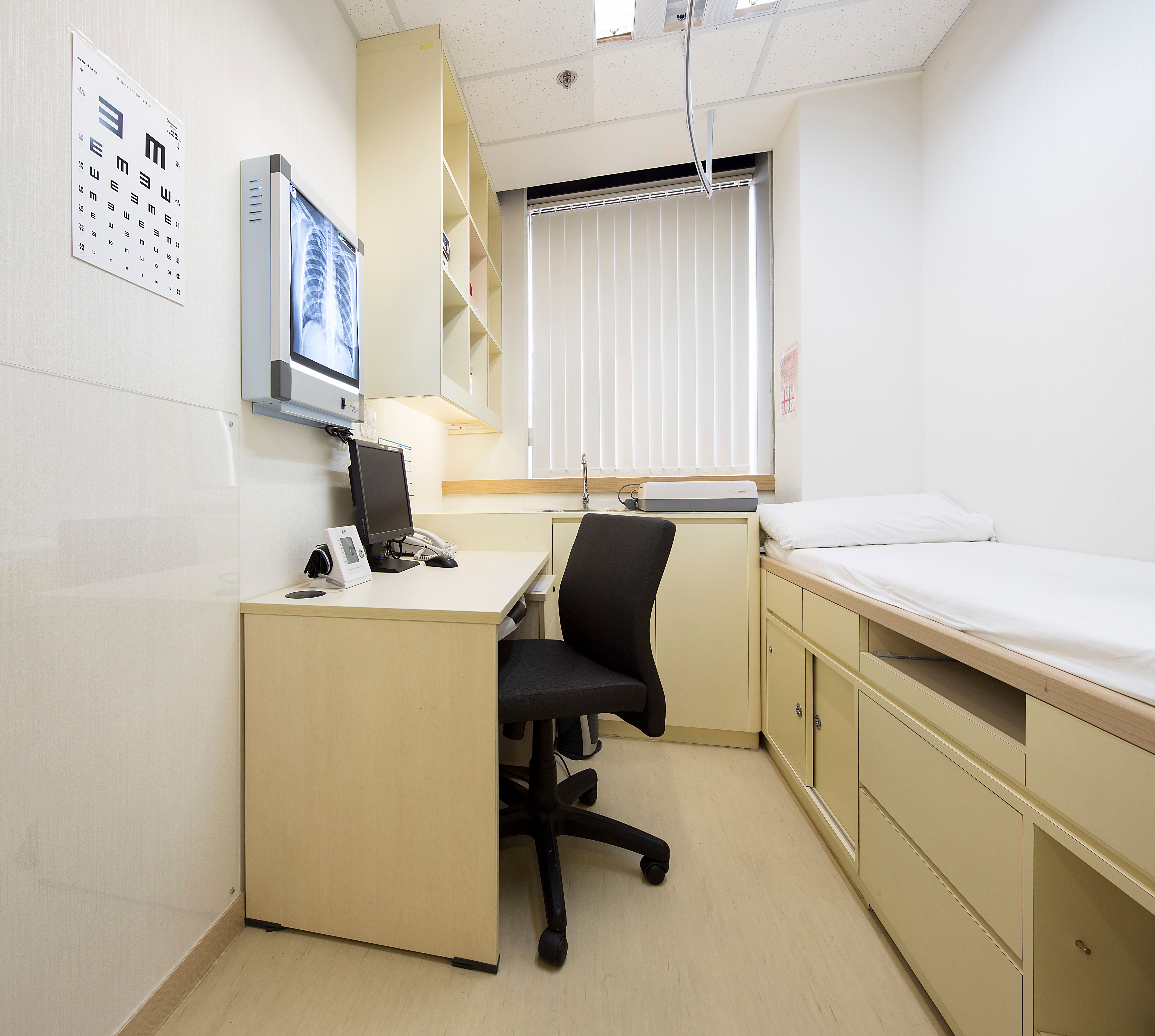 Examination room with patient bed, desk, wall eye chart, chest X-ray