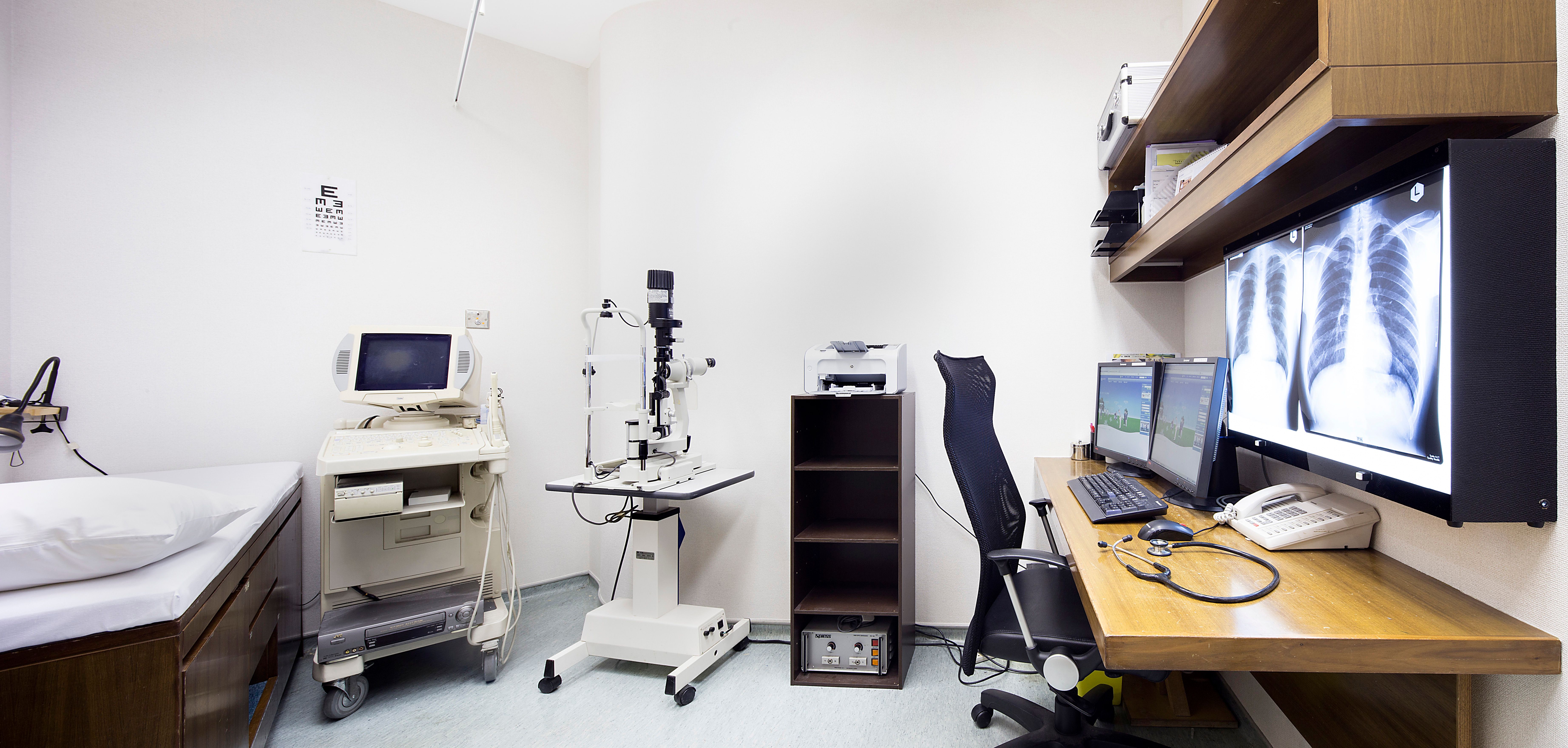 Examination room with patient bed, medical equipment, desk and X-rays