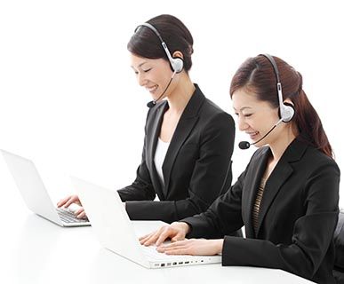 Two smiling female customer service workers seated at laptops wearing headsets