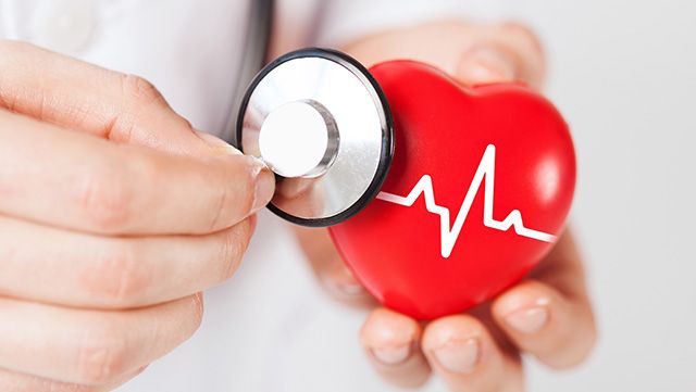 Hand holding stethoscope onto red heart