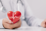 Close-up of doctor's hand holding a red heart with a superimposed heartbeat