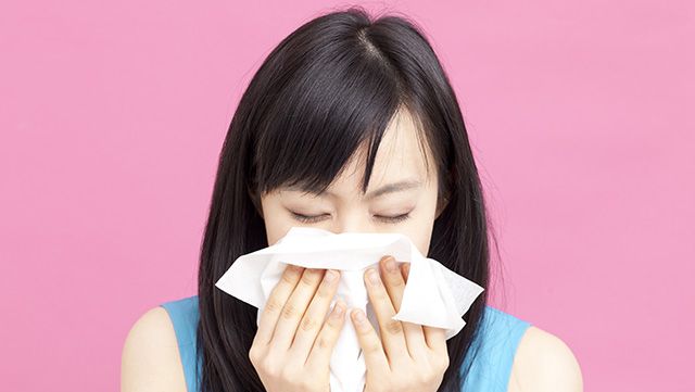 Woman covering her nose and mouth with tissues