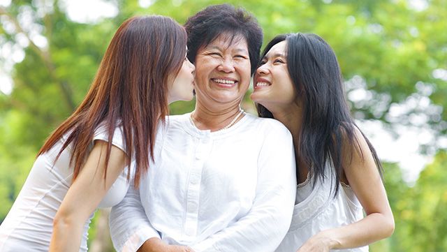 Two adult daughters kissing their mother's cheeks