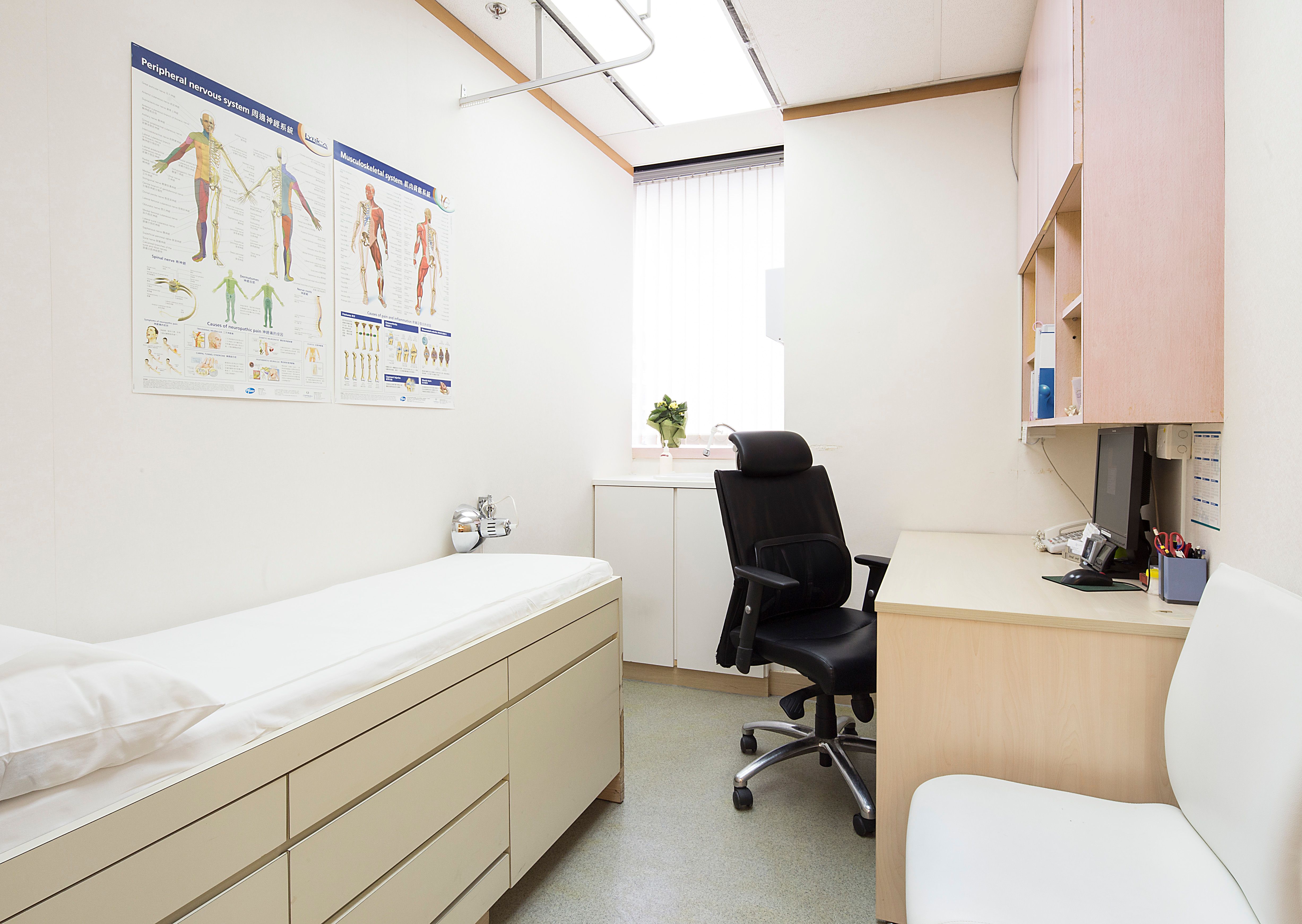Consultation room with desk, bed, anatomy posters on the wall