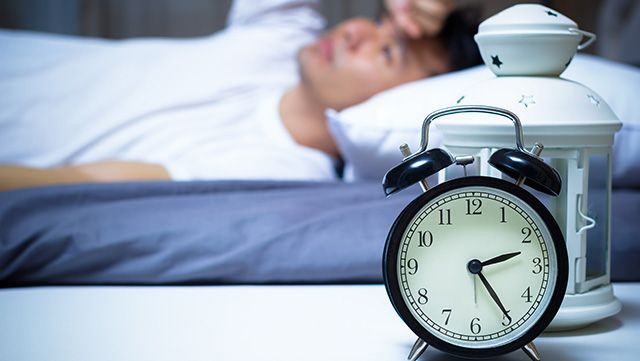 Alarm clock with man unable to sleep in the background