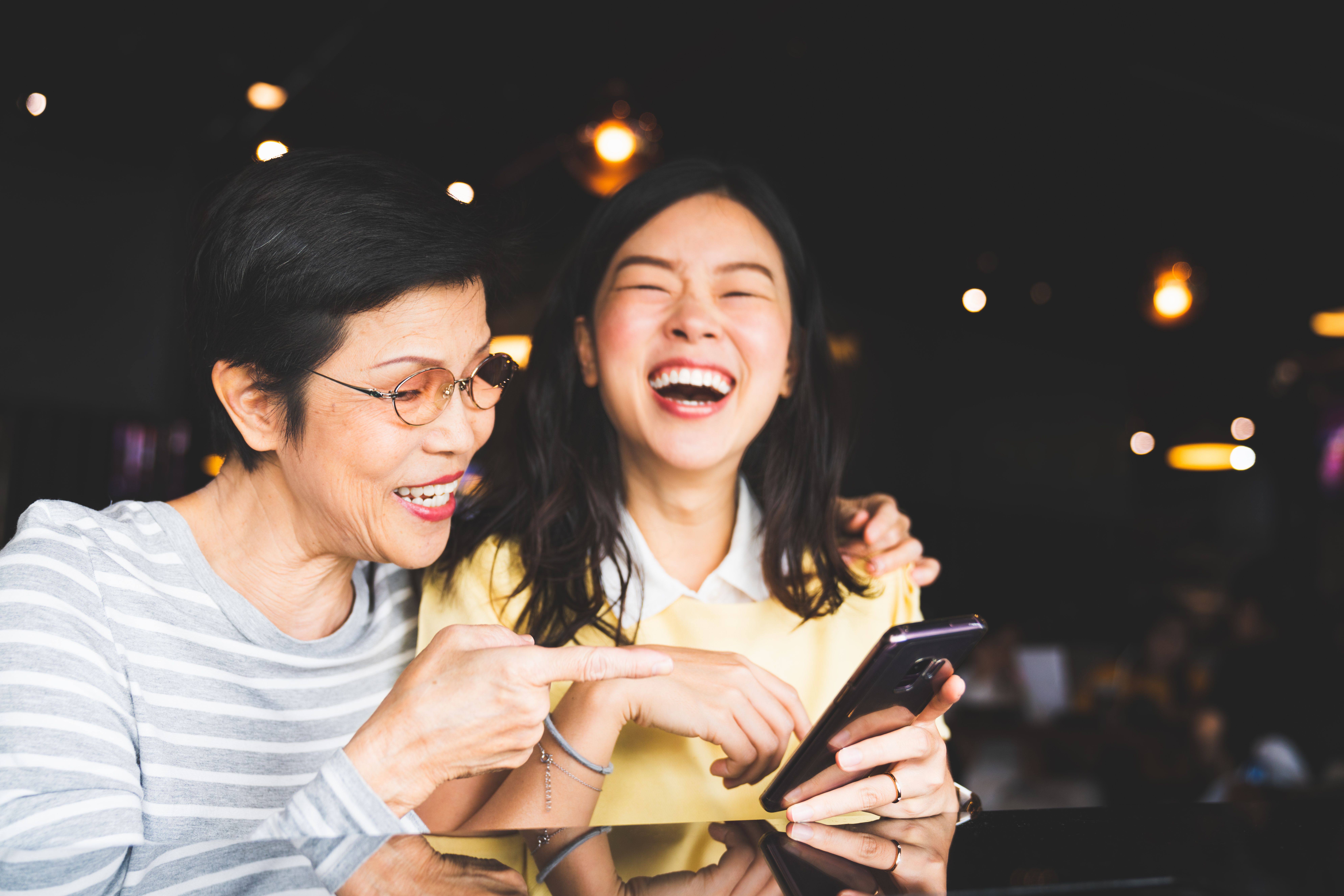 Elderly woman and younger woman looking at smartphone and laughing