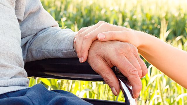Young hand touching the wrist of an elderly person in a wheelchair