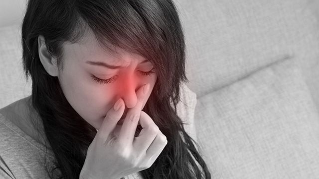 Woman holding her painful nose with right thumb and forefinger