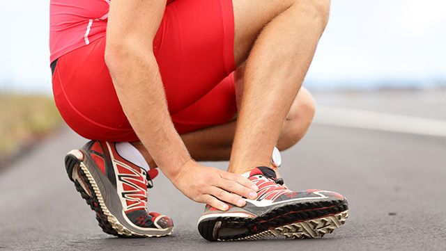 Close-up of a male runner kneeling down with an ankle injury