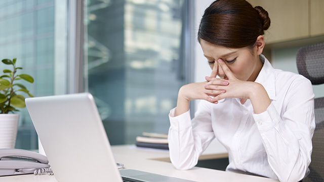 Office worker sitting at a desk leaning her head into her hands