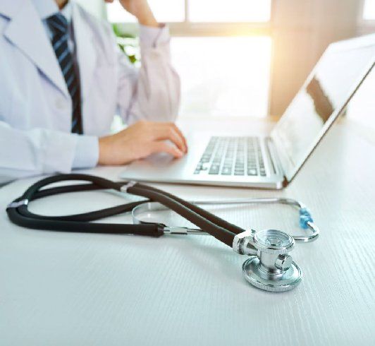 Doctor using a laptop on a desk with a stethoscope