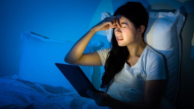 Woman pinching nose bridge while reading tablet in dark room