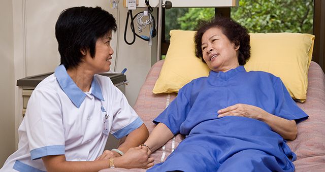 Nurse talking with an elderly female patient lying on a bed