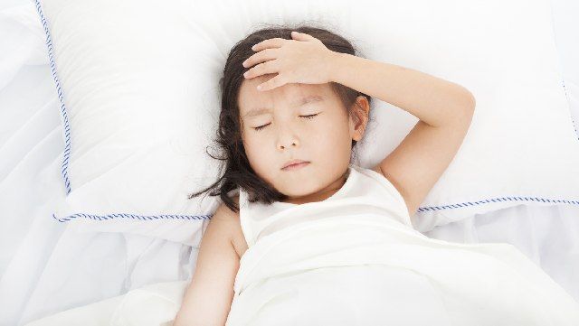 Young girl lying in bed with eyes closed and her hand on her forehead