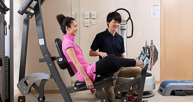 Physiotherapist helping patient use gym equipment