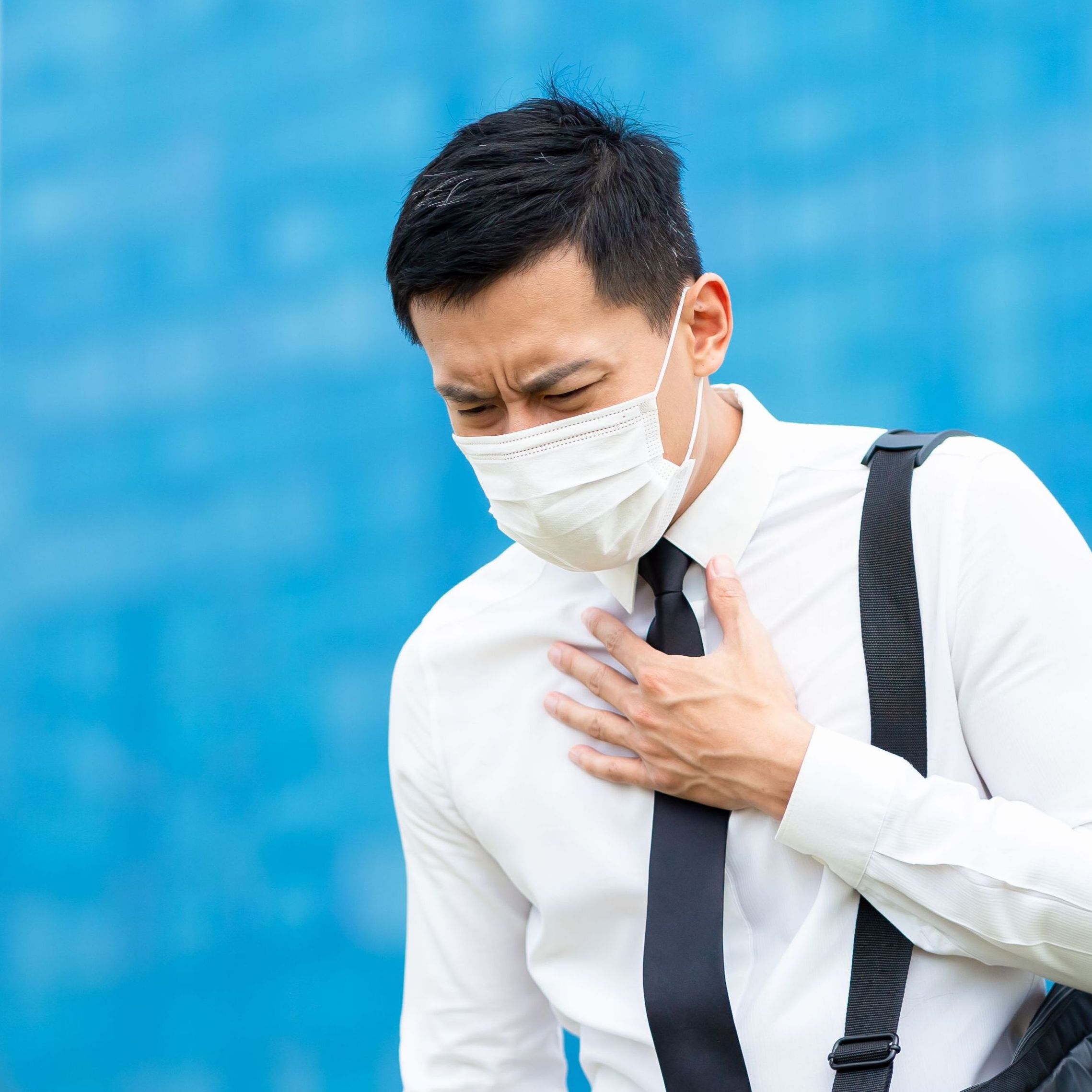 Masked businessman holding his upper chest and coughing