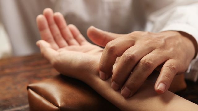 Traditional Chinese medicine practitioner evaluating patient's wrist