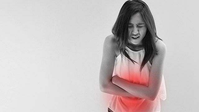 Black-and-white image of a woman with arms crossed over her painful abdomen